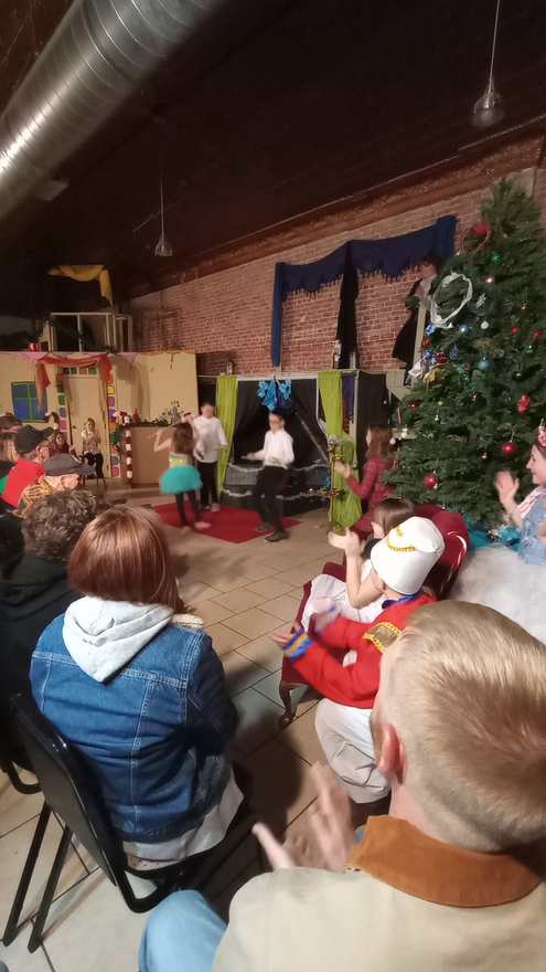 The audience applauds, the Nutcracker seated in red among the children in white tutus