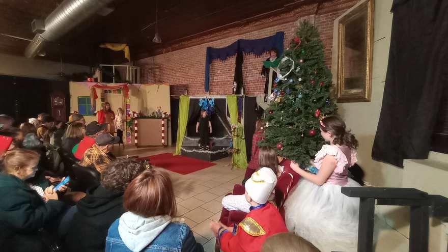 The performer in the tutu dress watches from the sofa as the scene plays across the studio