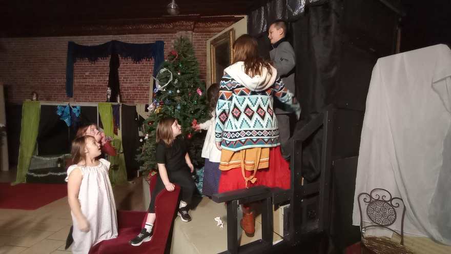 Backstage after the scene — young cast members in costume with an adult by the draped set pieces
