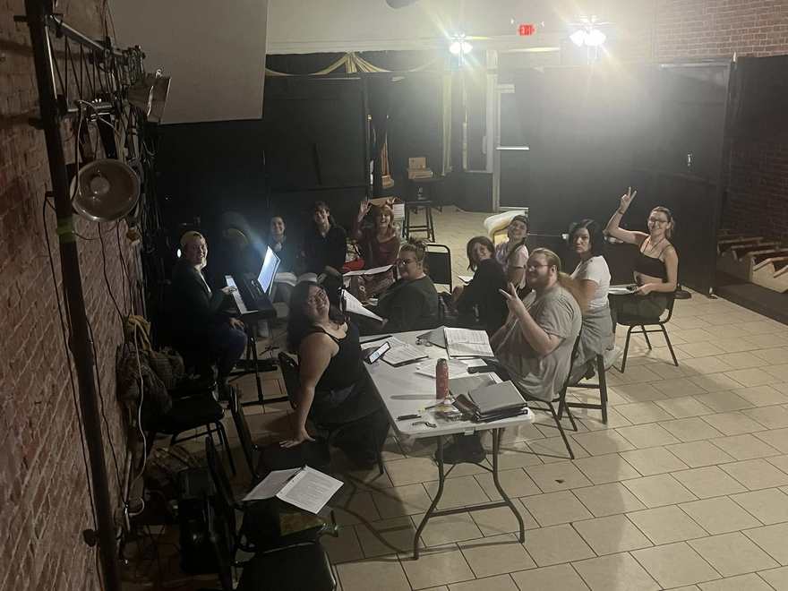 The Firebringer cast around the studio tables during rehearsal, scripts out and one hand raised