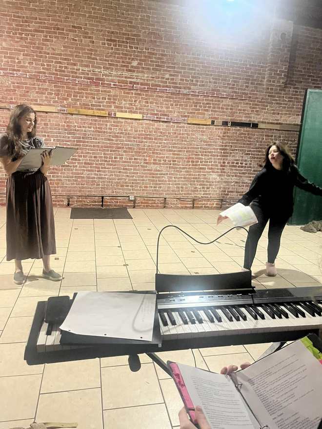 Two Firebringer performers rehearse with scripts behind the keyboard in the studio