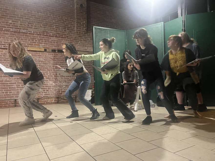 The Firebringer ensemble rehearses a crouched, creeping line of choreography, scripts in hand