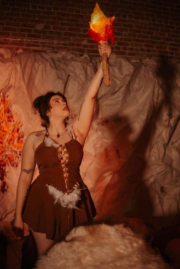 Zazzalil raises a flame torch high before the painted cave wall in Firebringer