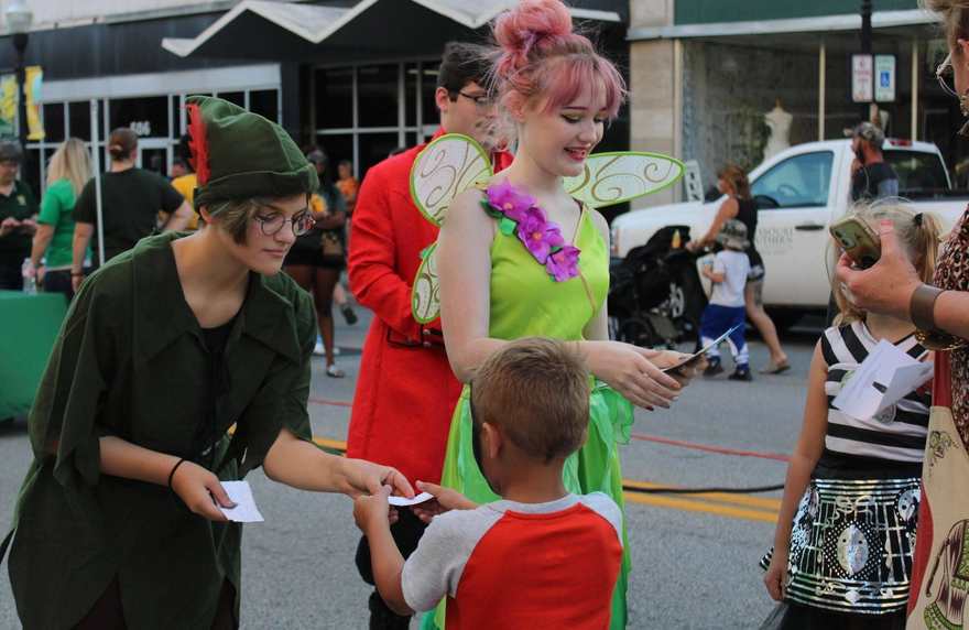 Costumed performers — Peter Pan and Tinker Bell — greeting young fans at a downtown street event